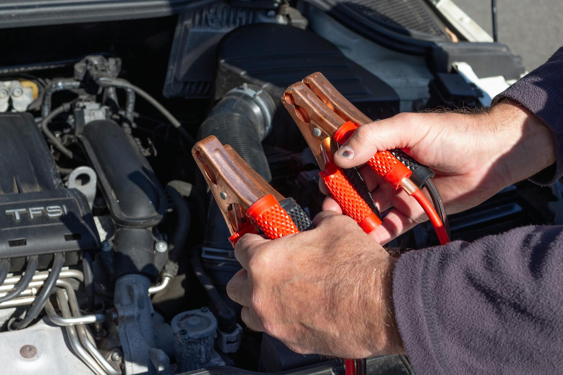 Man Holding Clips in Front of a Car Engine 
